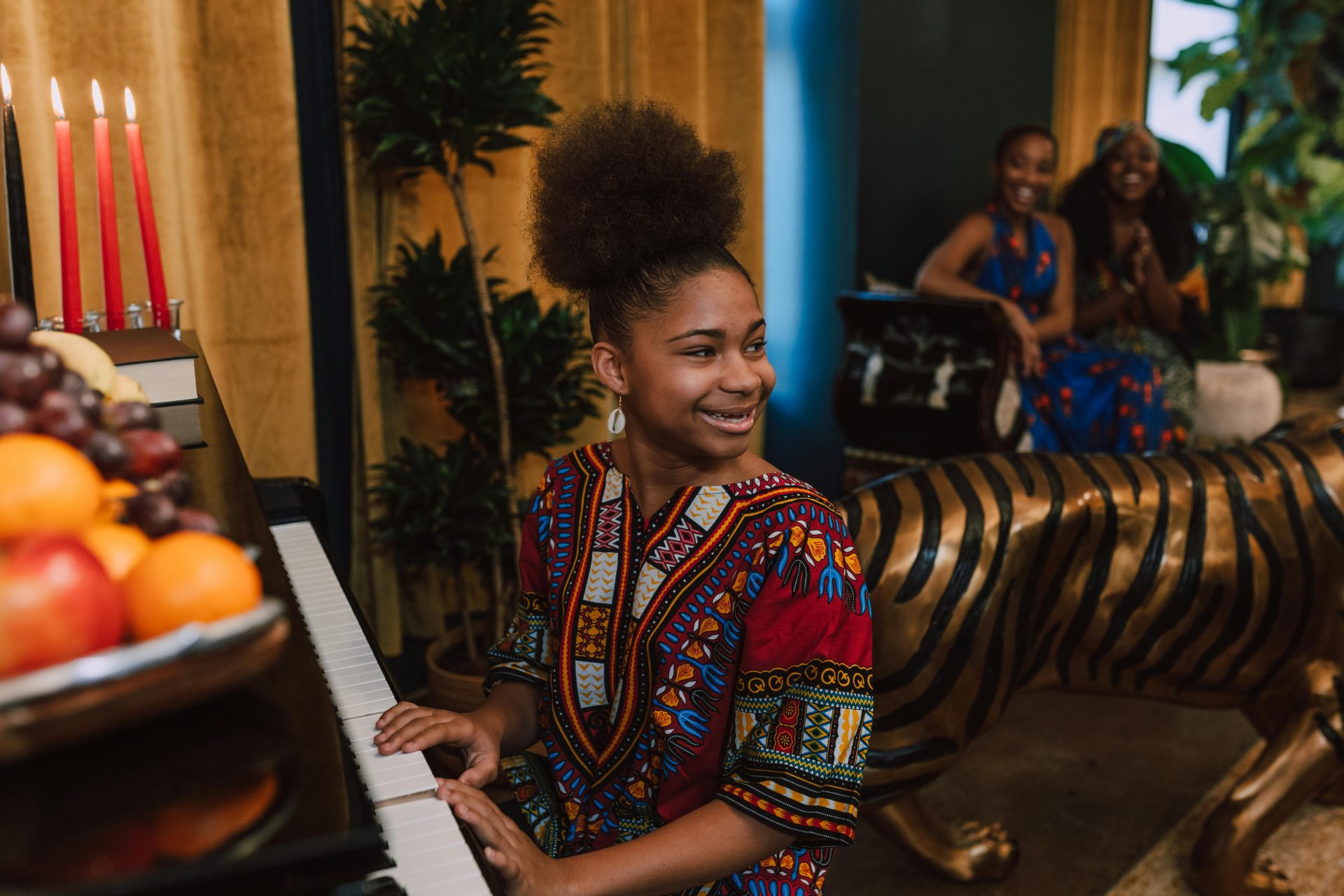 African American girl playing piano during a Kwanzaa celebration indoors, creating a joyous atmosphere.
